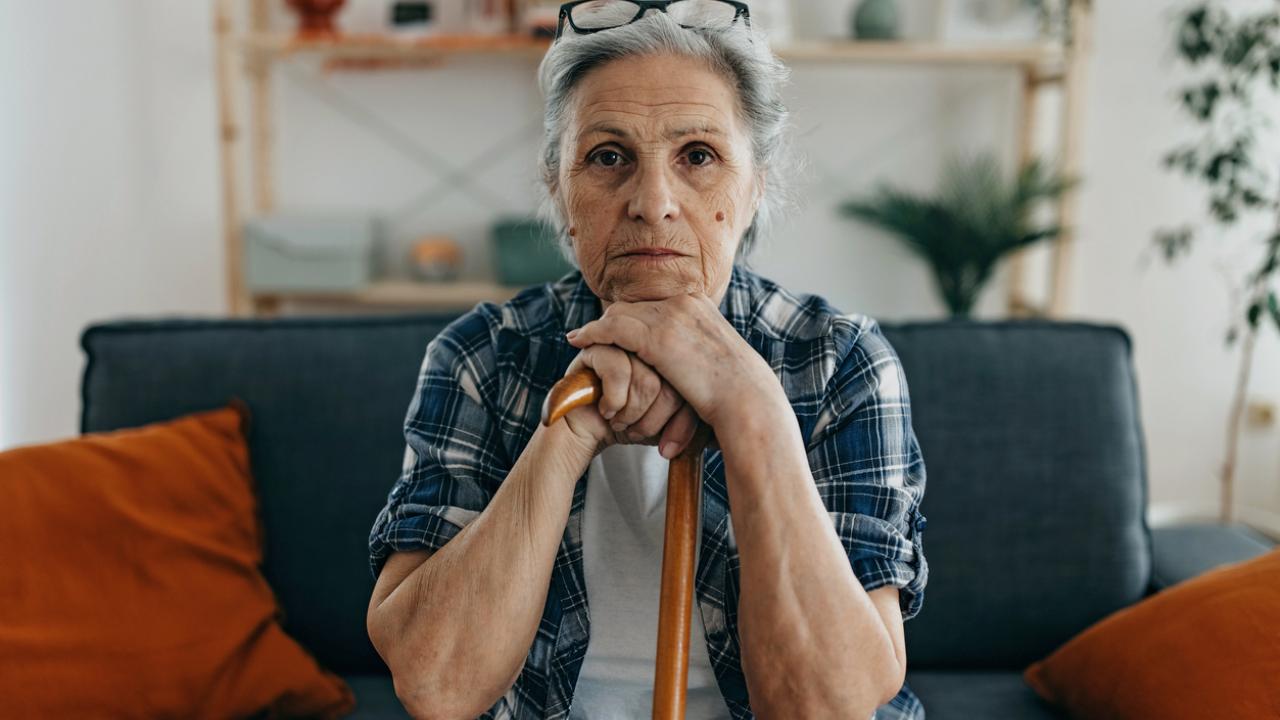 Woman seated on a couch holding her cane.