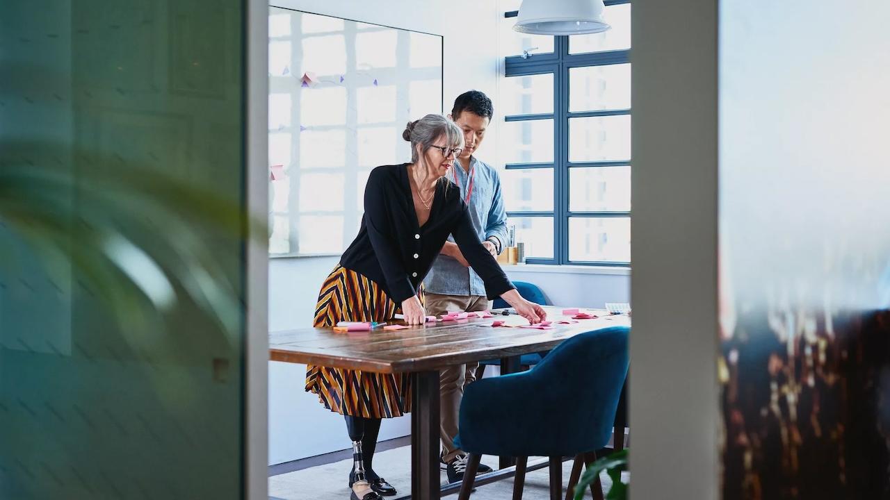 Two people at a table looking at a garment. The female has a prosthetic leg.
