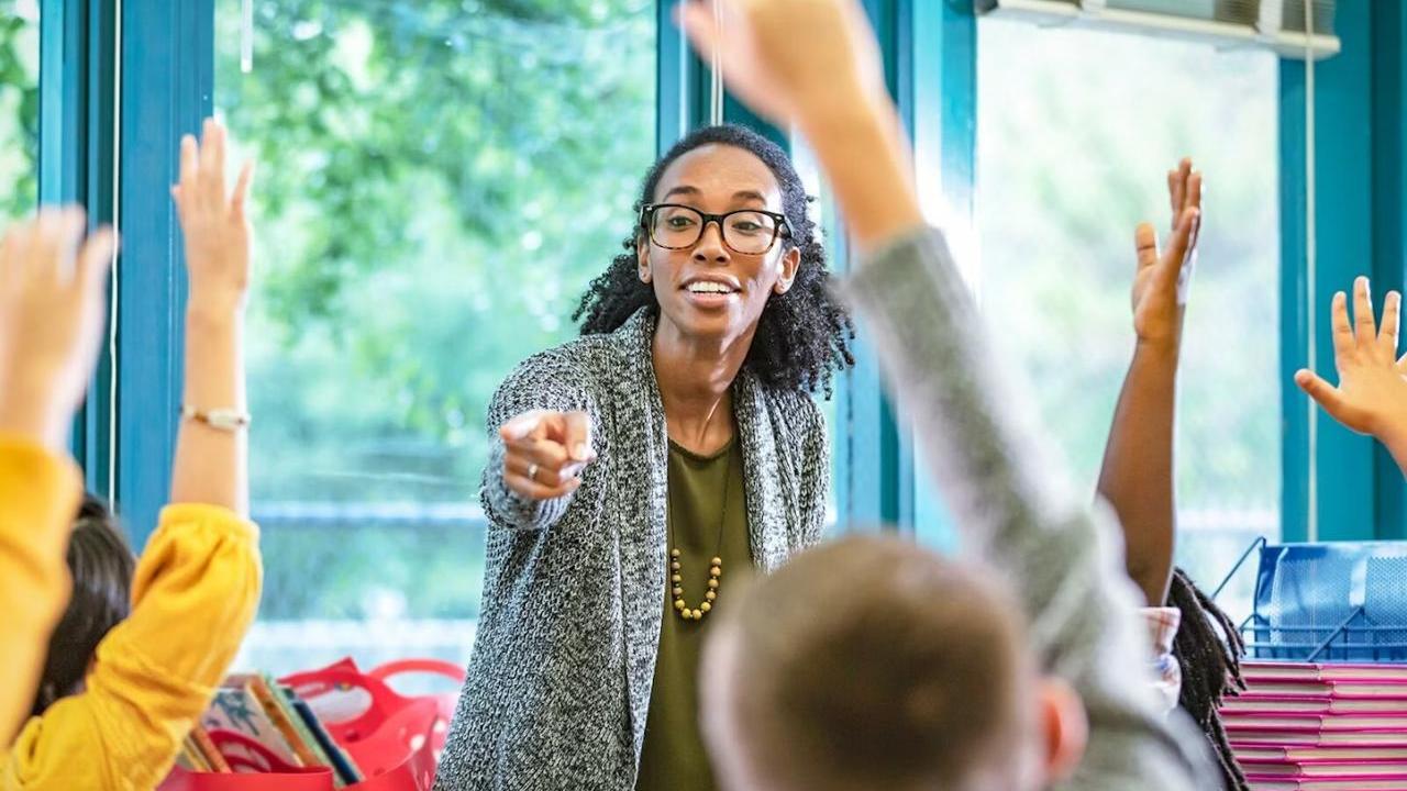 A teacher pointing to students with their hand raised 