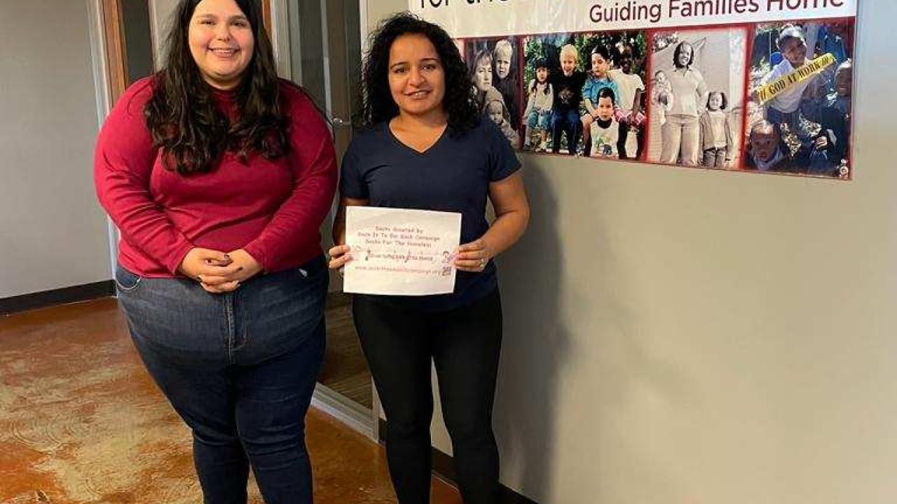 Two people standing behind donation to Foundation for the Homeless
