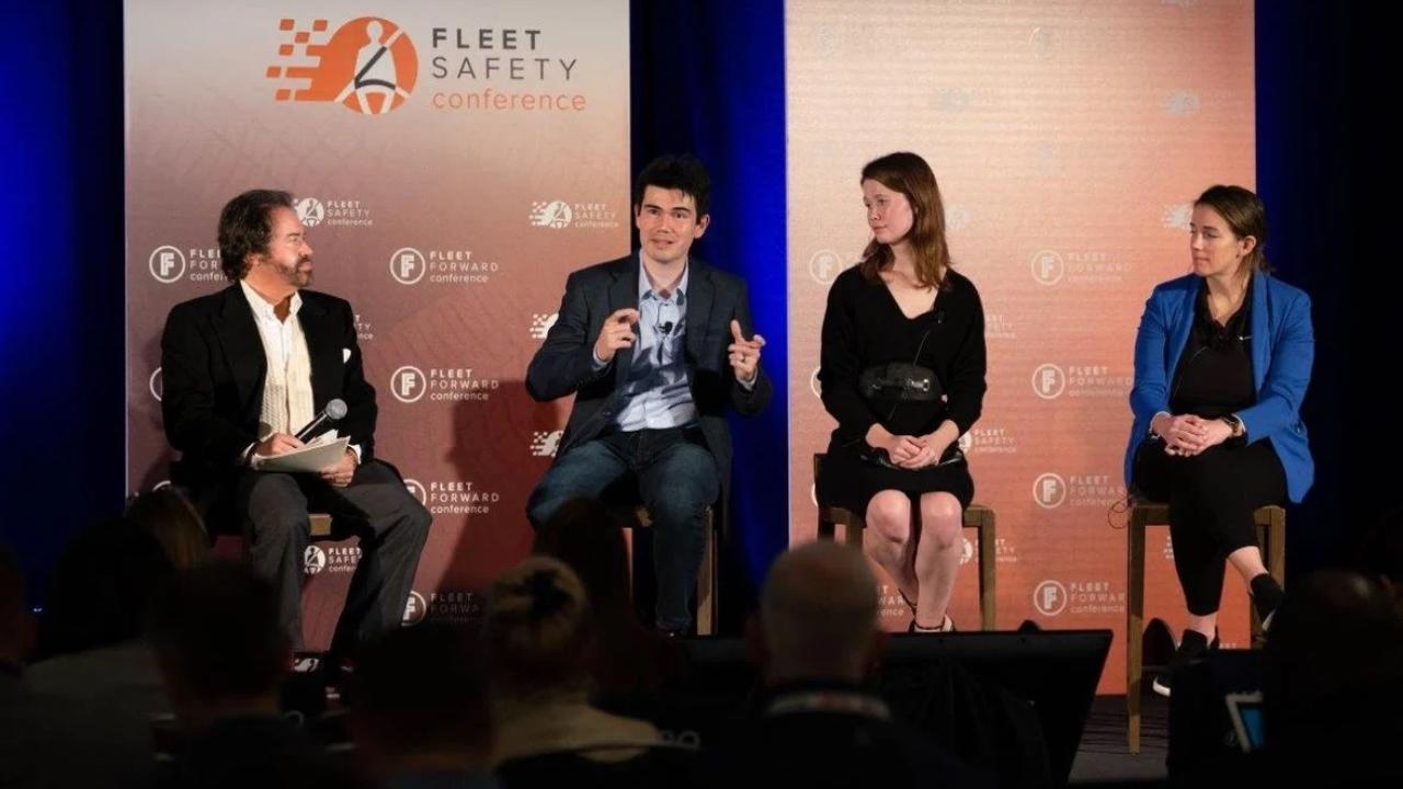 Frank Mycroft and the other panelists sit on stage in front of an orange backdrop.