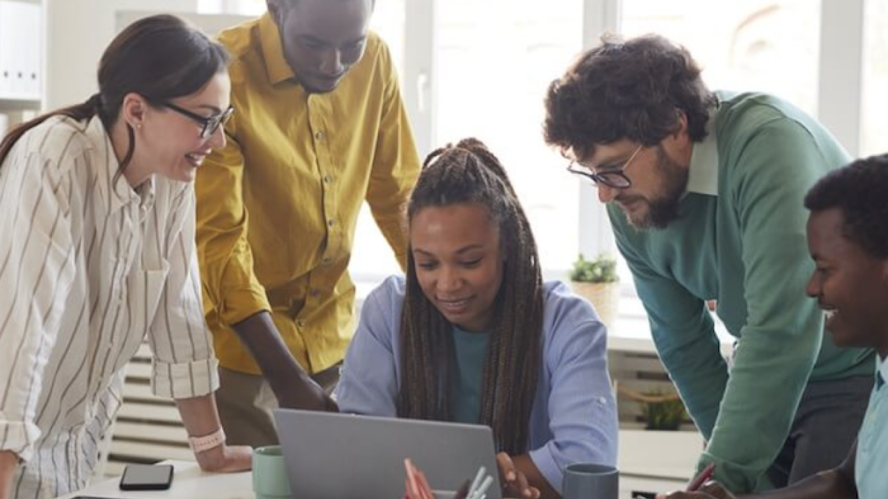 Five people seated around a laptop having a discussion.