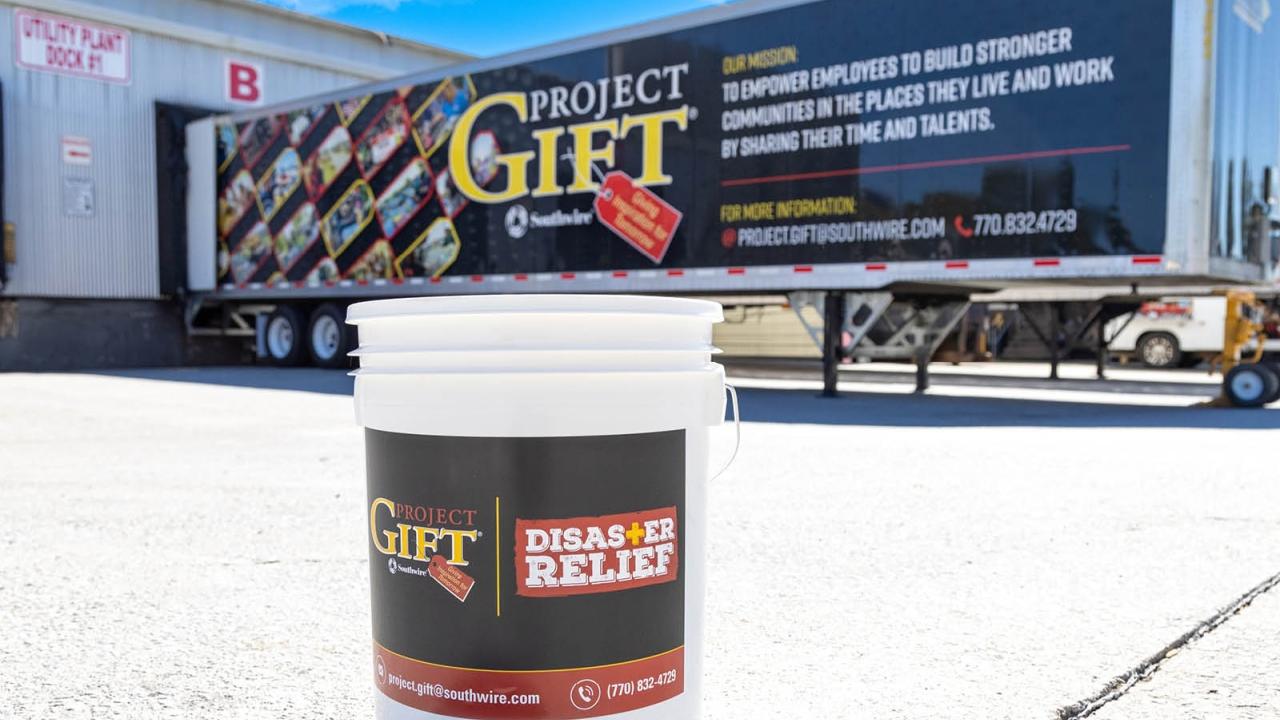a white bucket with "GIFT disaster relief" label. A trailer in the background with "Project GIFT" on the side