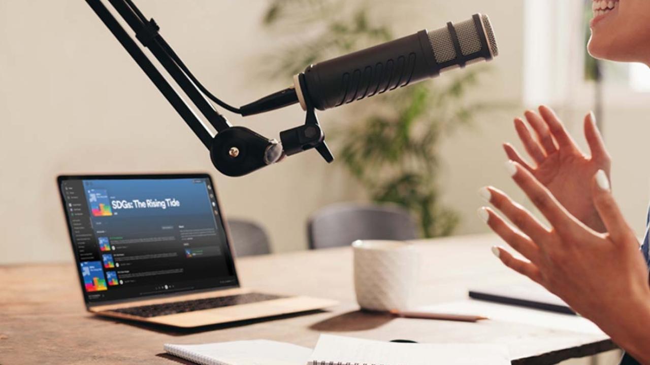 person speaking into microphone with laptop next to them on a desk