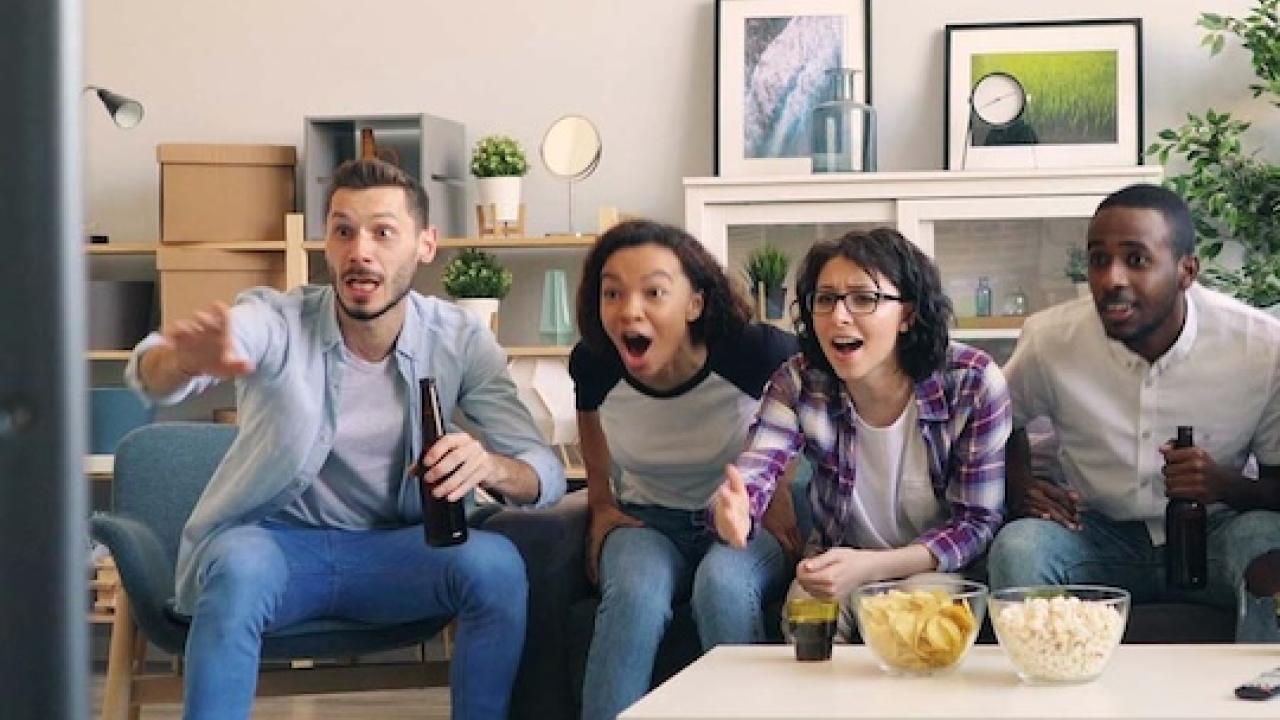 Four people watching tv while seated on a couch.