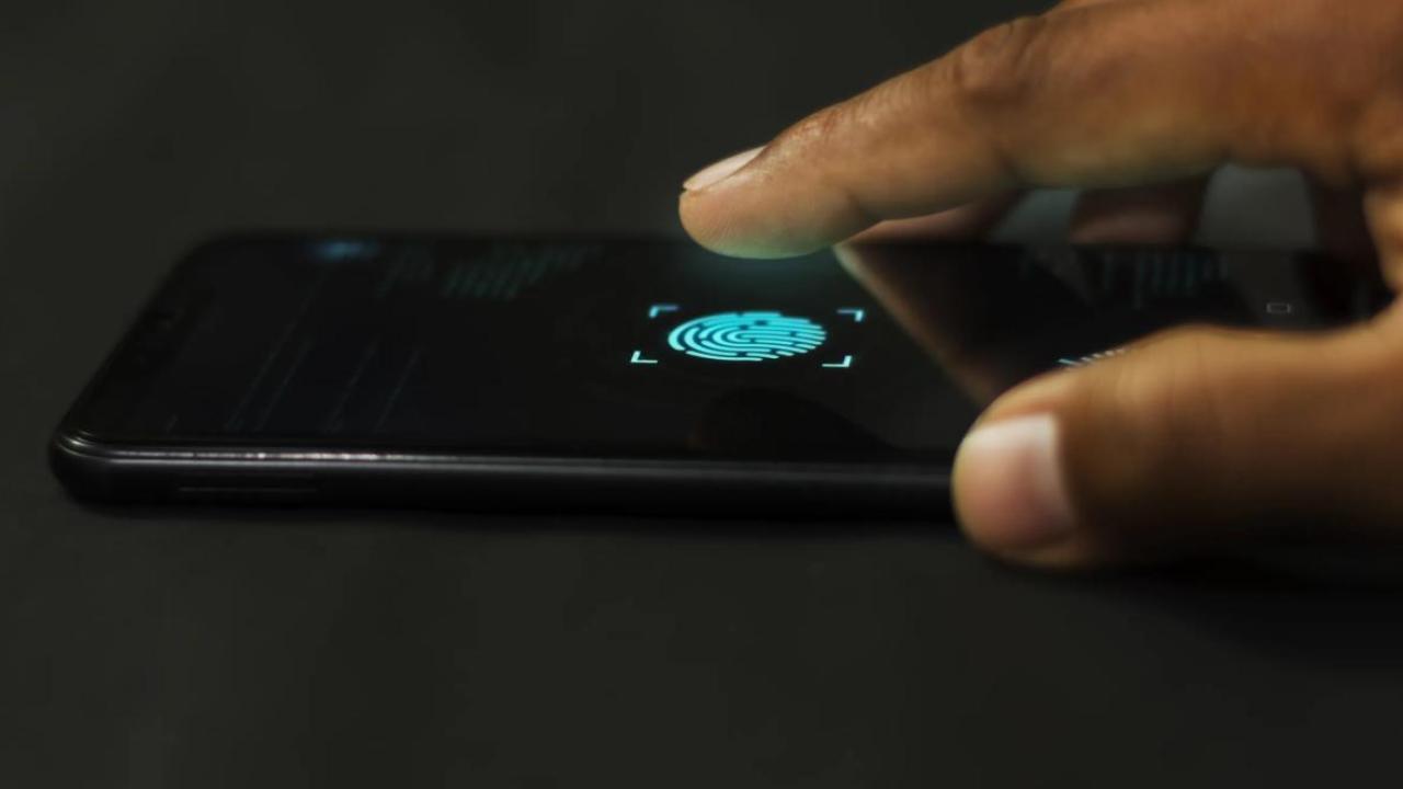 A close-up of a finger poised to tap a fingerprint scanner icon on a smartphone screen, indicating biometric authentication.