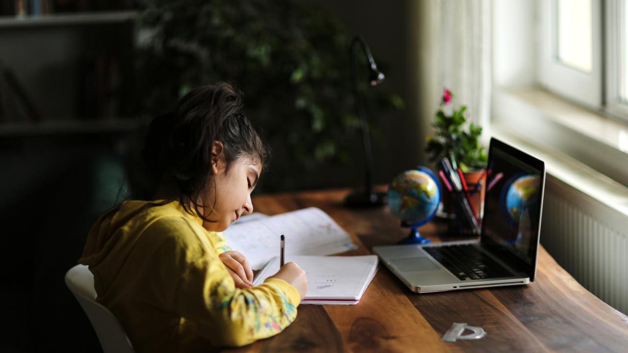 student writing on paper in front of a laptop