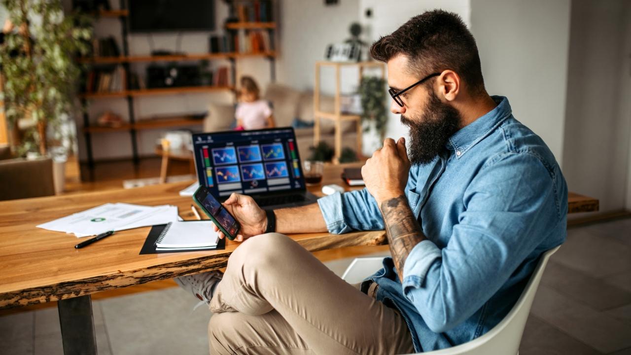 bearded man sitting at a desk looking at smartphone