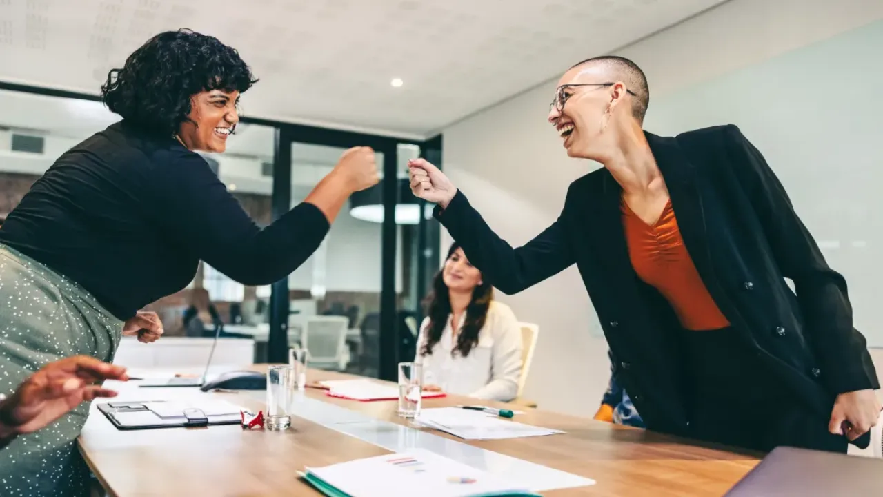 Two diverse colleagues smile and fist bump during a meeting, symbolizing support, inclusion, and positive workplace culture.