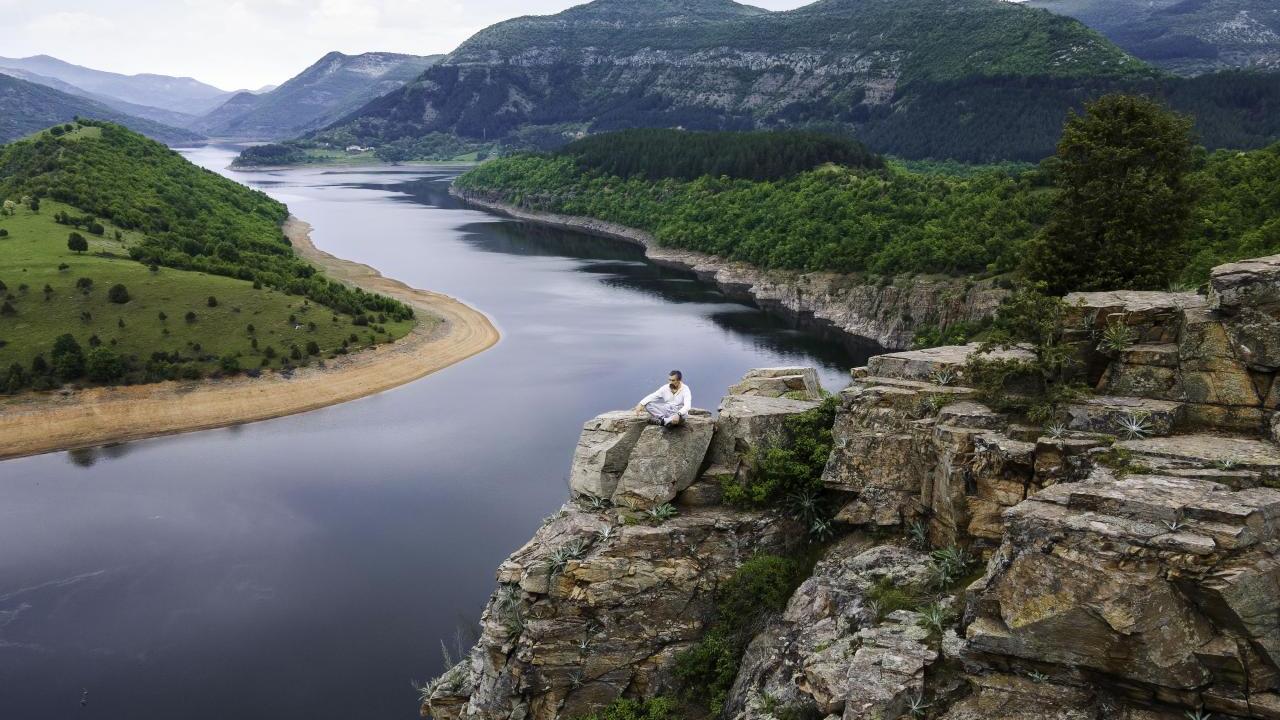 A person seated on a tall rock overlooking a winding river.
