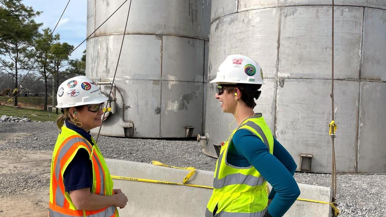 Two women stood talking to each other wearing hi-vis vests and safety hats 
