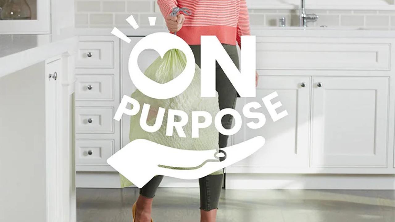 A person carrying a trash bag in a kitchen. "On Purpose" logo on top.