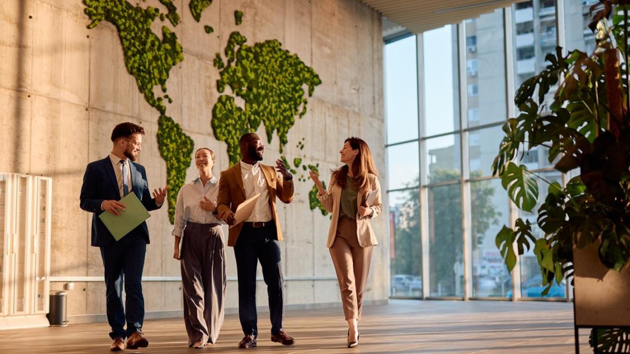 Team walking and chatting in an office building with a map of the world in the background