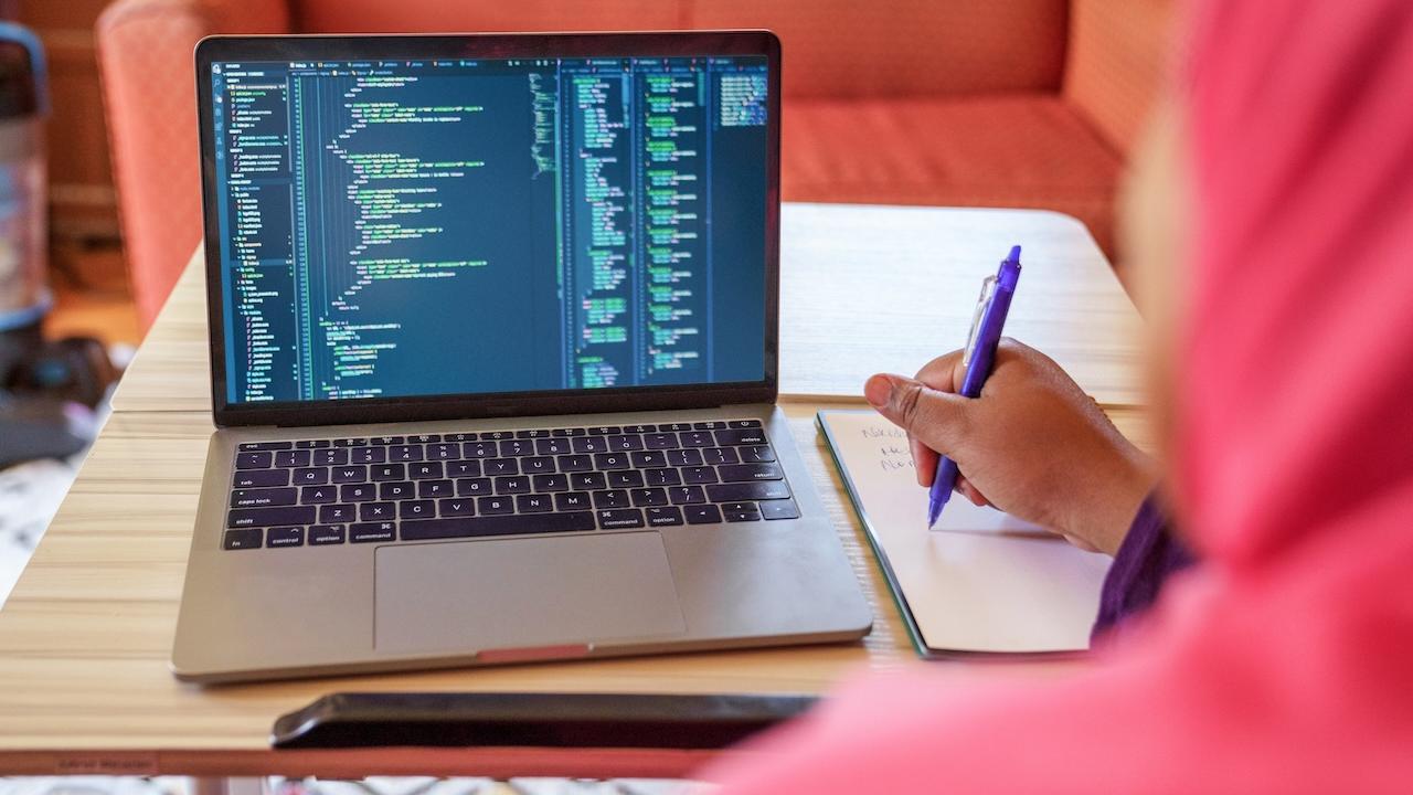A person seated at a desk in front of a MacBook.