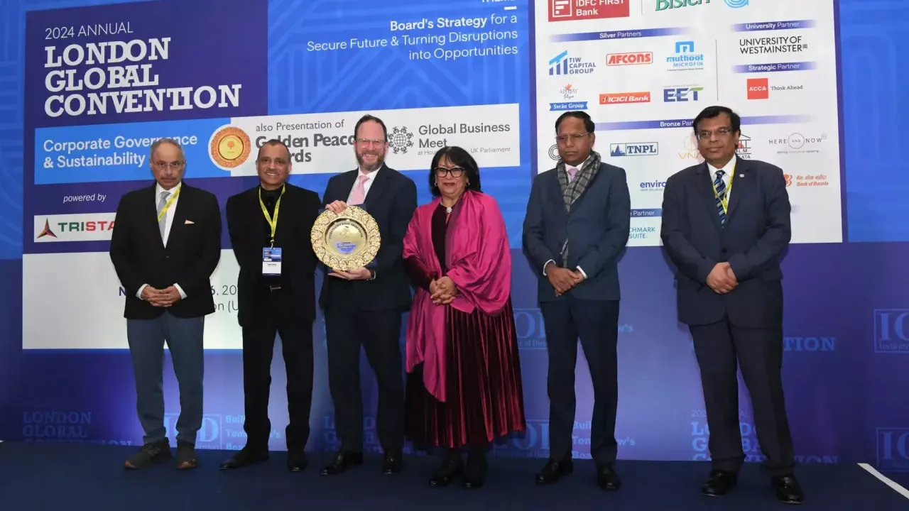 Six people posed in front of a large display "London Global Convention" One holds a golden award.