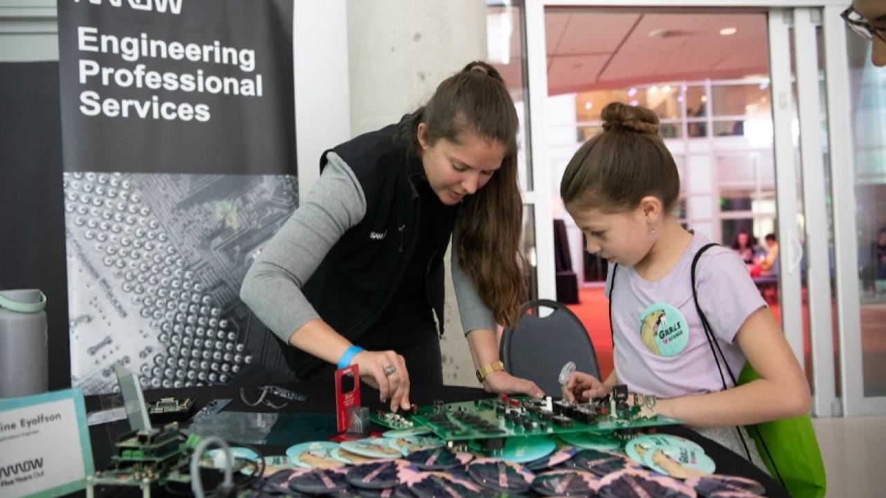 Grace Doepker at an Engineering professional services stand showing a young child some equipment