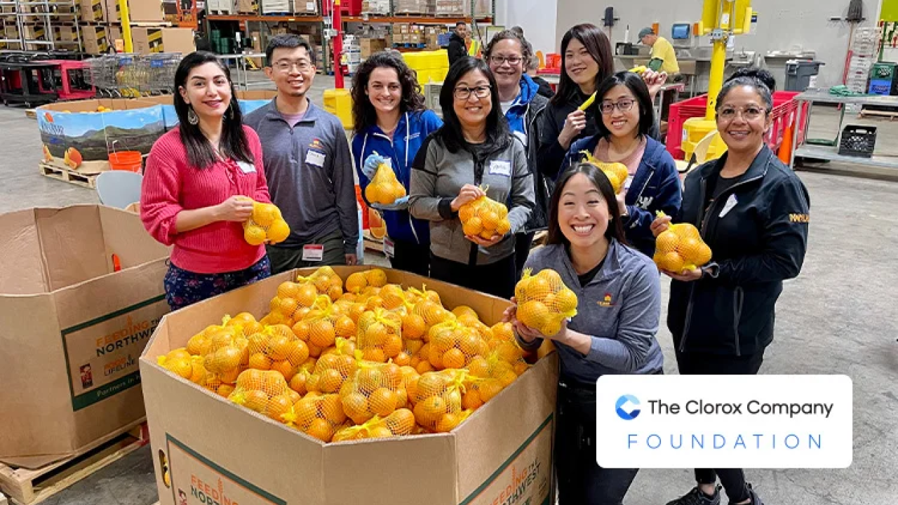 Smiling group of people standing around a pallet of oranges