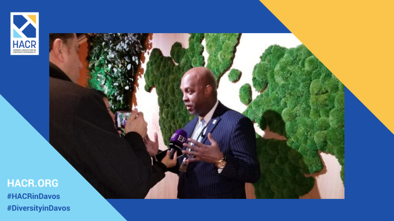 Photo of Cid Wilson, President and CEO of the Hispanic Association on Corporate Responsibility dressed in a suit speaking into a microphone with a textured, green and white wall in the background