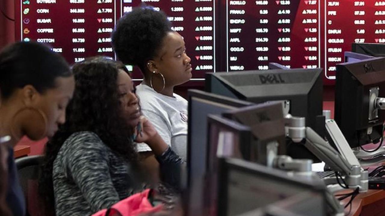 Female people of color sit in a classroom behind computer screens.