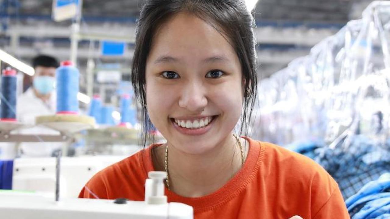 Female worker, smiling, behind a sewing machine.