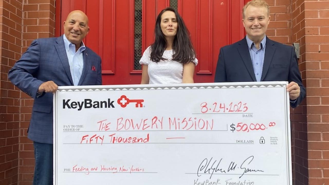 Representatives from KeyBank and The Bowery Mission shown holding a grant check for $50,000.