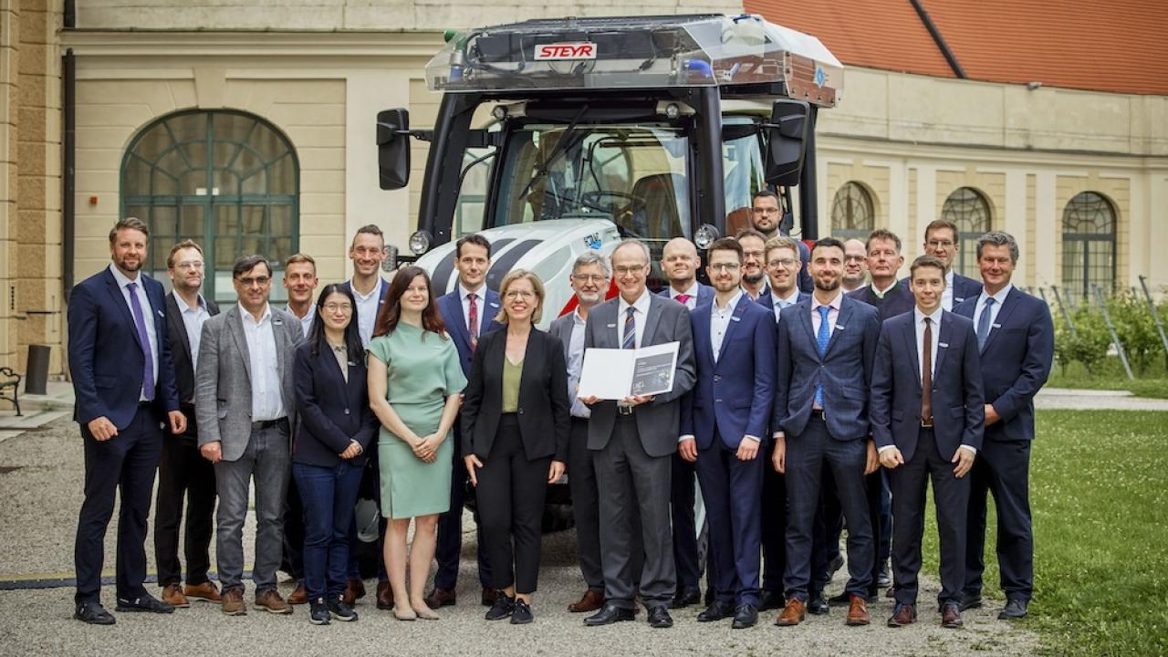 Group of people in formal attire standing outside in front of large tractor