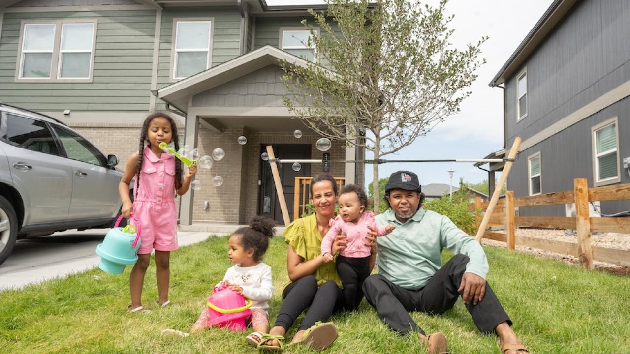Family of parents and three children sitting in front of house blowing bubbles