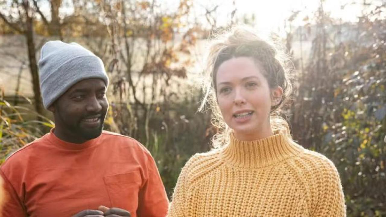 A person in a yellow-knit jumper talking to a group of people