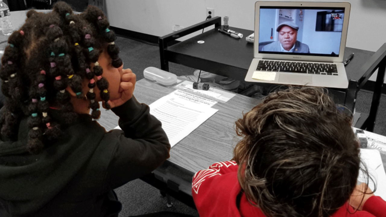 two students at a desk watch a video on a laptop