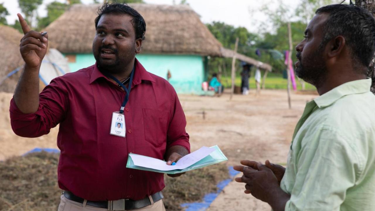 a person wearing a name badge and holding papers points away, another person in front of them