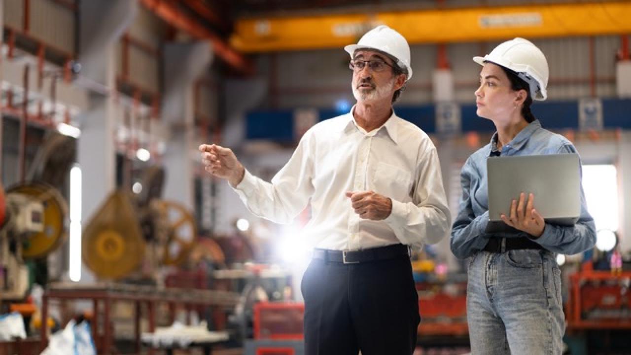 Two people wearing hard hats speaking in a workshop