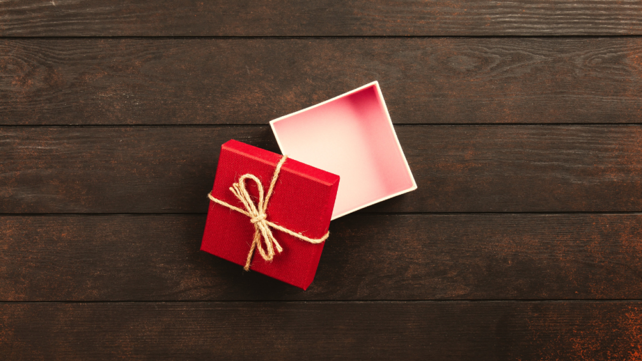 A small, red, square gift box sits opened on a dark wooden table.