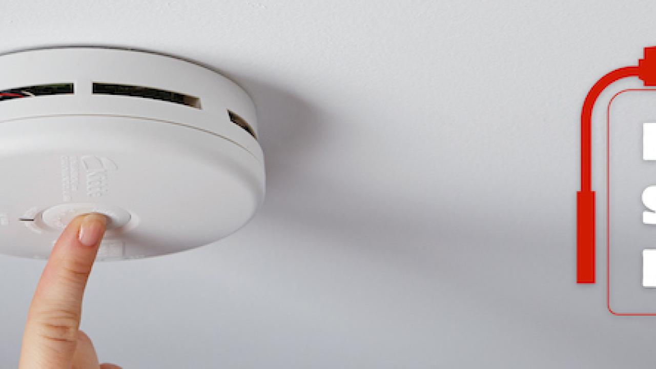 Fire Safety Month: Finger shown pushing the button on a smoke detector.