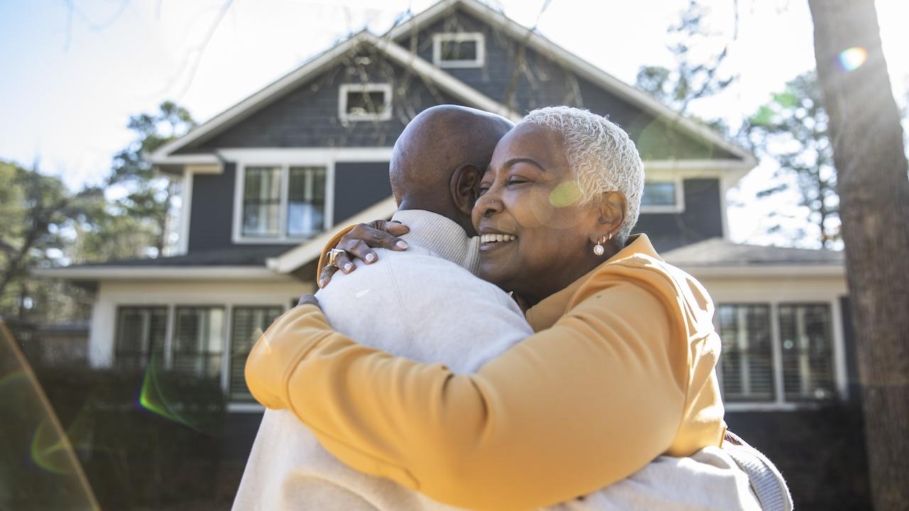 Older couple hugging outside of their new home.