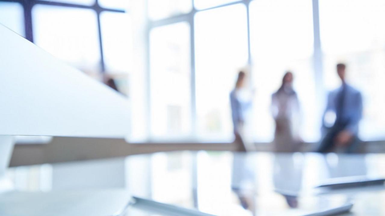Blurred photo featuring three people in the back of a well-lit office space