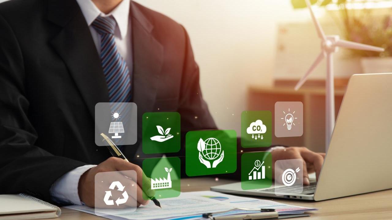 Business employee working at desk with sustainability related symbols in foreground