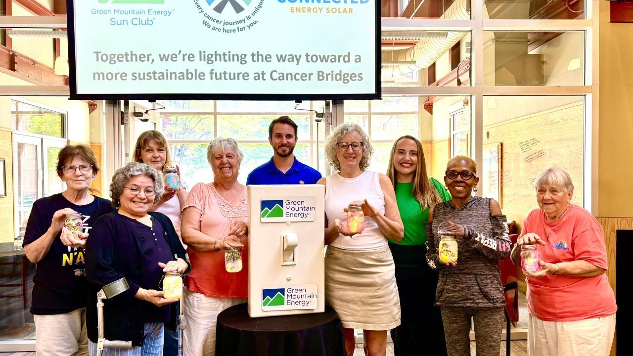 Members from Cancer Bridges, Connected Energy Solar, and Green Mountain Energy Sun Club smiling with solar mason jars and a life-size light switch.
