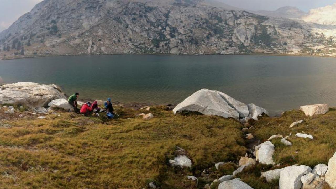 People at the edge of a body of water in mountainous terrain.