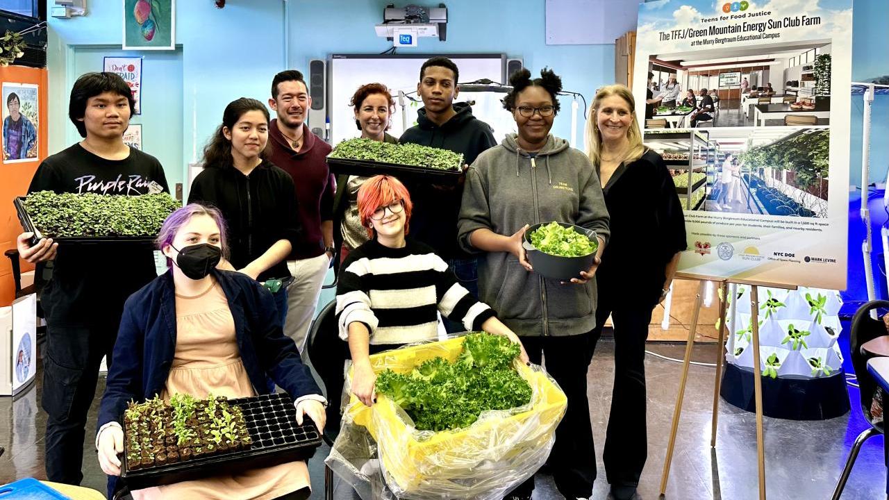 Students and organizational members pose in a high school classroom in front of hydroponic farm setup.