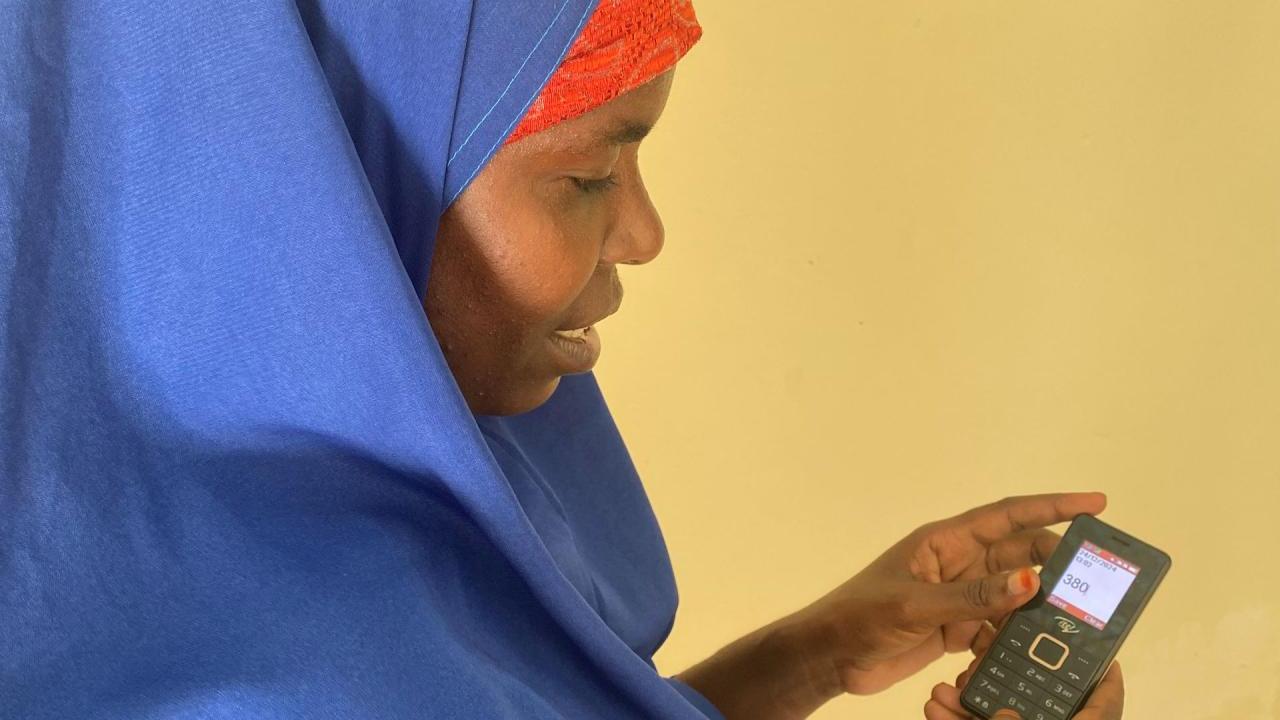 A woman holds a small cellphone in front of a yellow wall. 