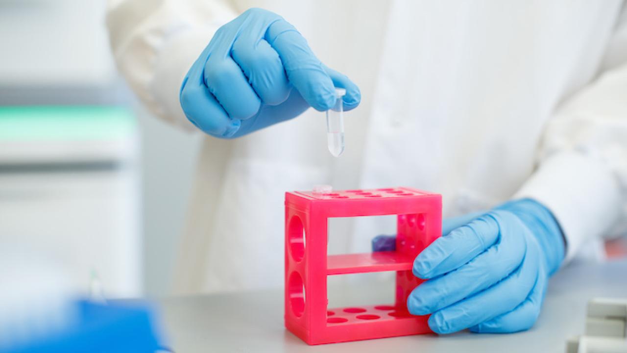 Illumina scientist; gowned and gloved removes a test tube from a rack.