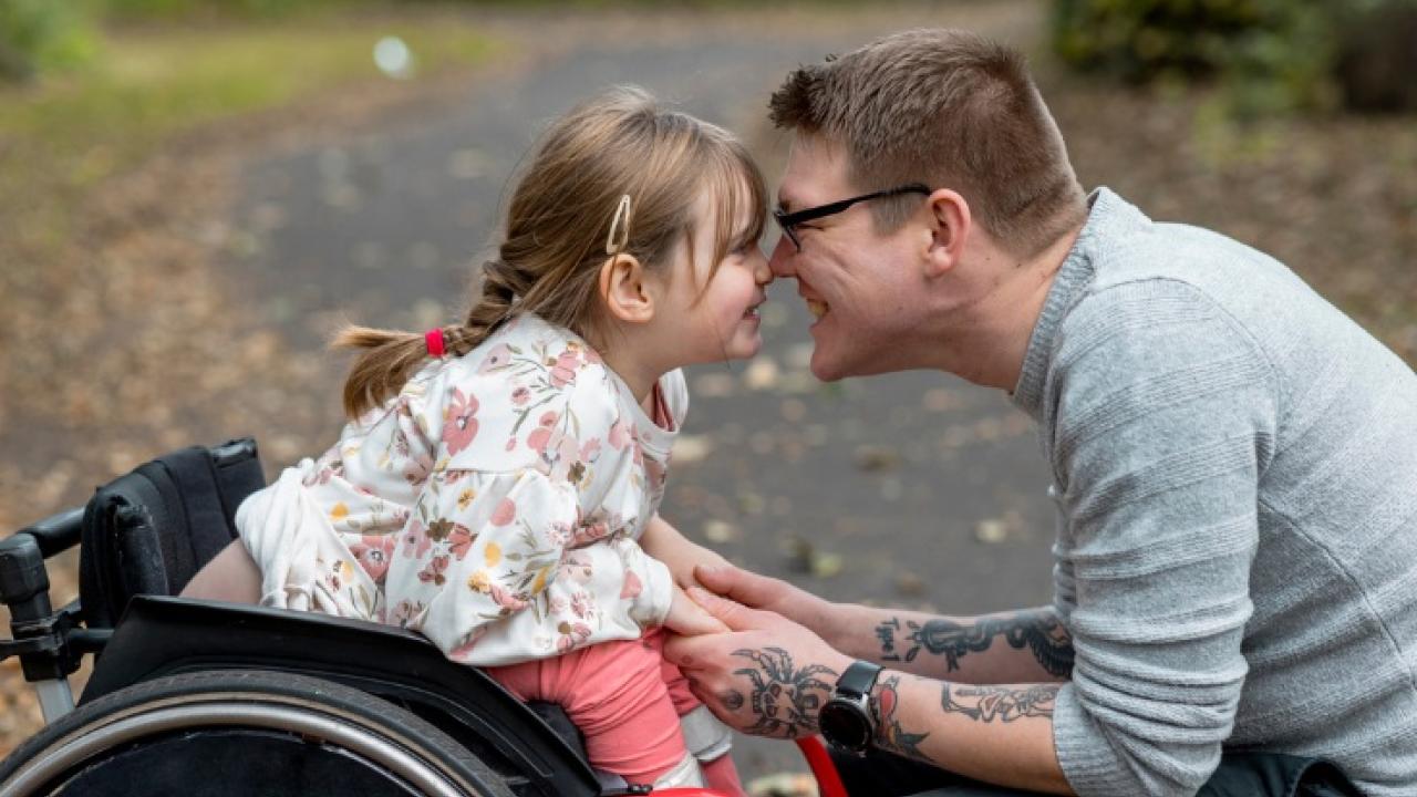 Young girl in a wheel chair with her dad hugging her.