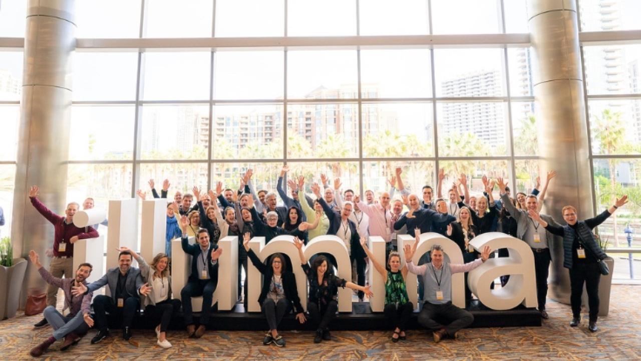 Illumina employees seated in front of the Illumina logo in the corporate headquarters.