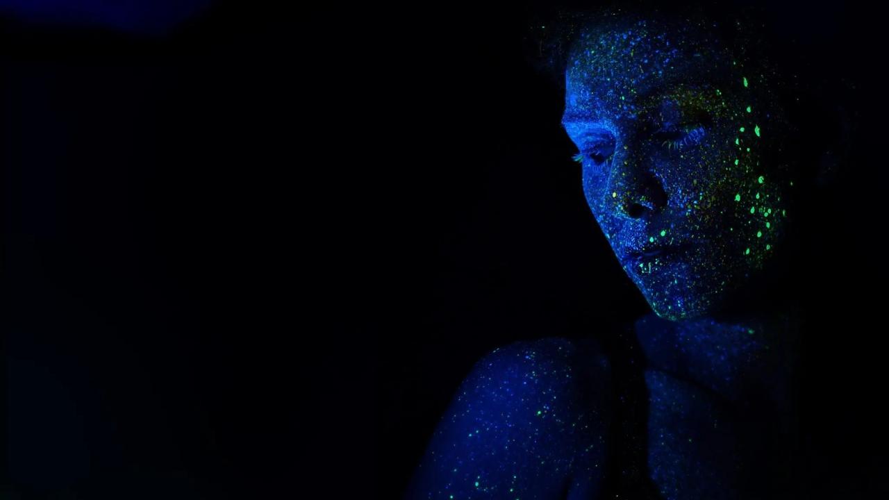 a dark space, a face lit by blue-light on the right, green paint spatters on the face