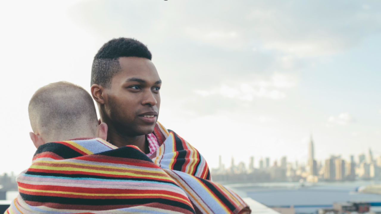two people standing close together in front of cityscape, wrapped in one scarf