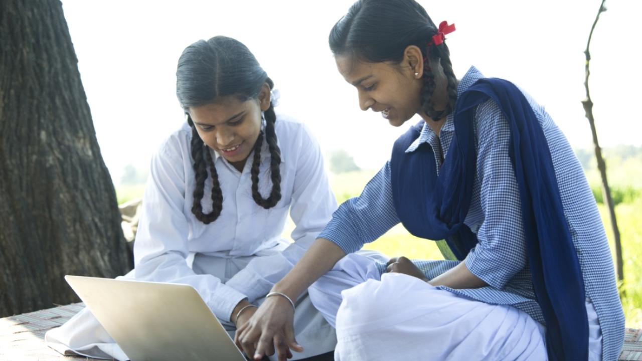Two children outdoors under a tree looking at a laptop screen
