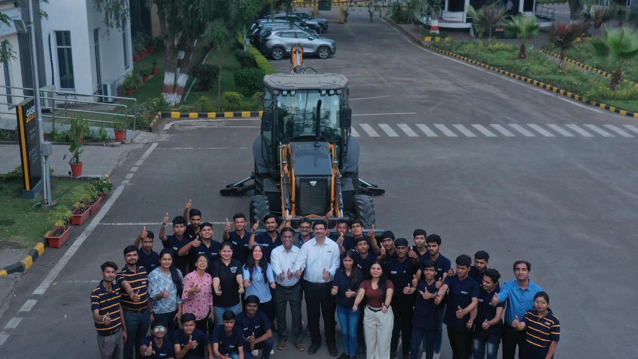 Aerial view of a group of people posed in front of large tractor, each giving 'thumbs-up'.