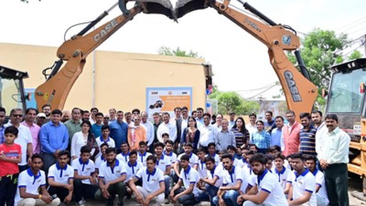 A group of people posed under two tractors with extended bucket arms.