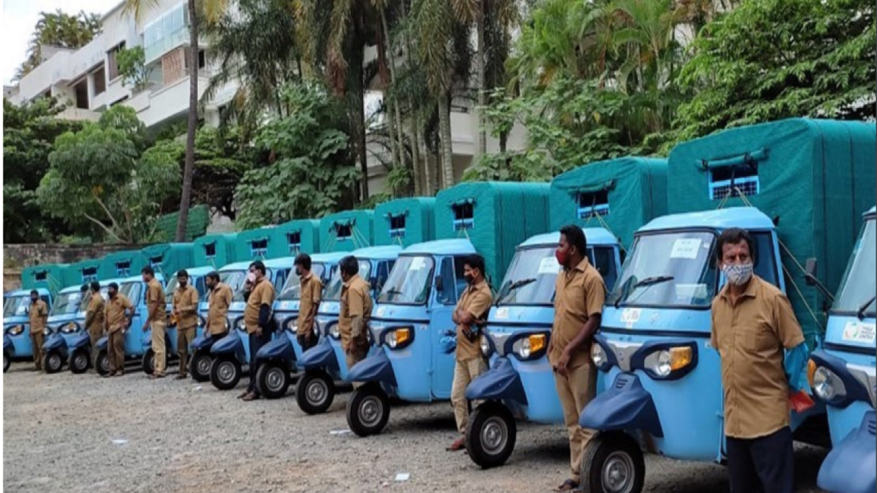A row of identical small vehicles with drivers standing to the side.