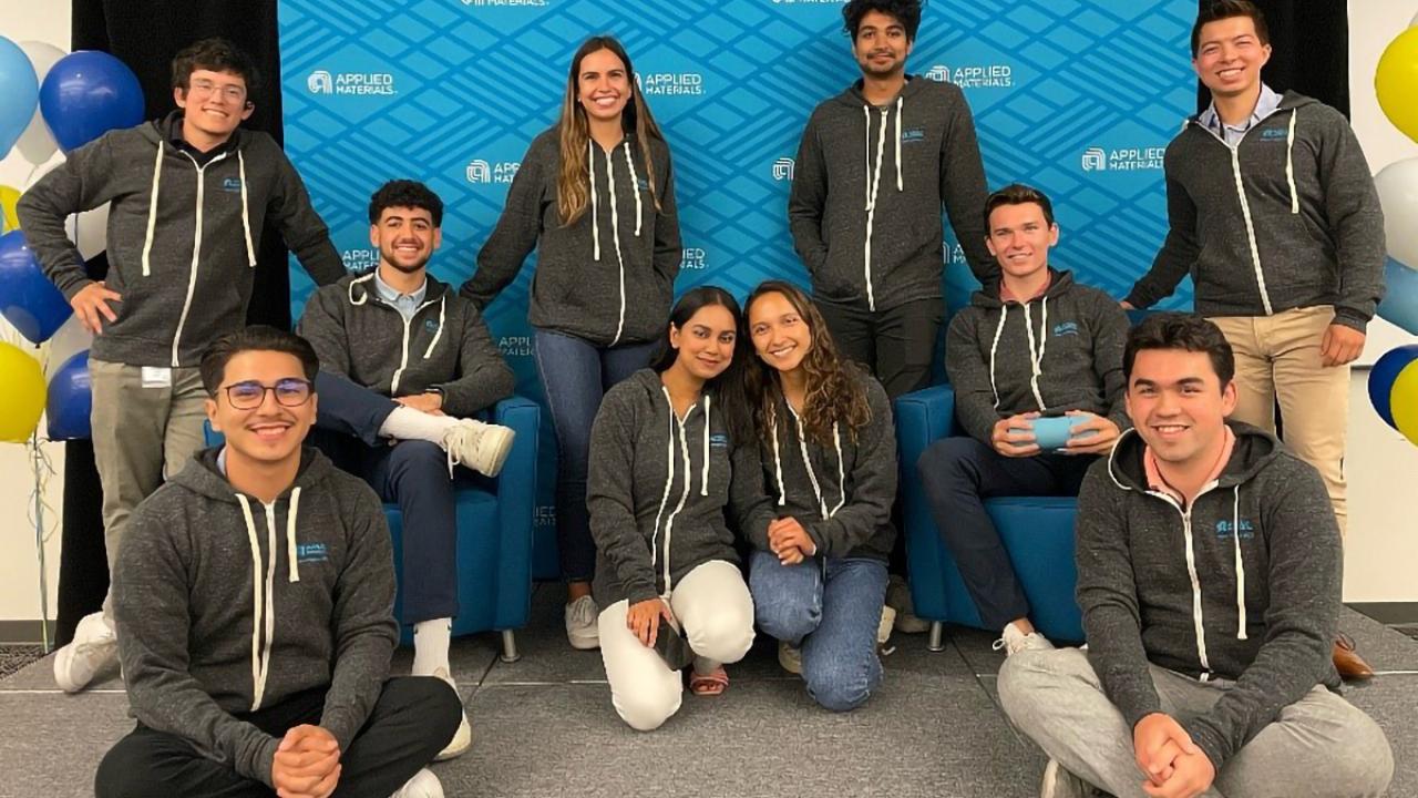 interns in gray hoodies pose in front of a blue applied materials logo wall